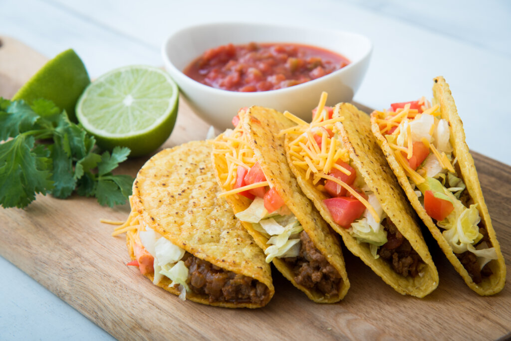 Picture of 4 tacos on a wooden board with limes and salsa
